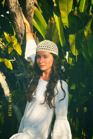 AZURE, singer and songwriter poses in tropical foliage with a white dress and knit cap.